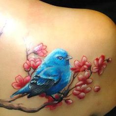 a blue bird sitting on top of a tree branch with red flowers around its neck