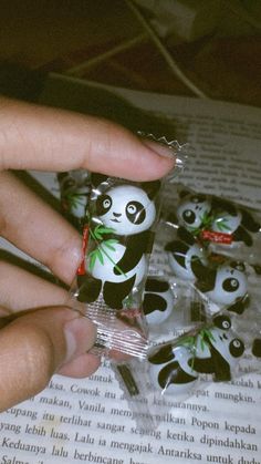 a hand is holding some little pandas in small packages on top of an open book