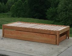 a wooden bed frame sitting on top of a cement floor next to a lush green field