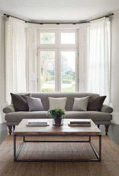 a living room with a couch, coffee table and large window in it's corner