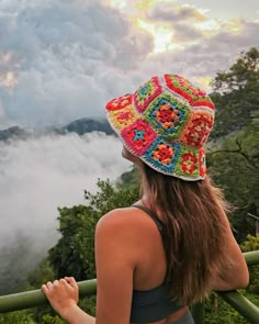 a woman wearing a colorful crochet hat looks out over the clouds on top of a mountain