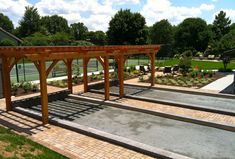 an outdoor tennis court with steps leading up to it and a pergolated area in the background