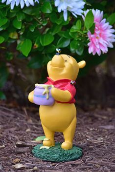 a winnie the pooh figurine holding a pot with flowers in the background