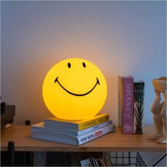 a yellow smiley face lamp sitting on top of a table next to books and a vase