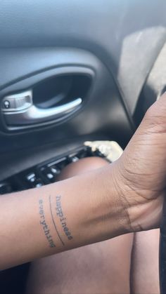 a person with a small tattoo on their arm in a car holding the steering wheel