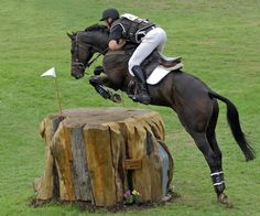 a man riding on the back of a horse jumping over a wooden stump in an open field