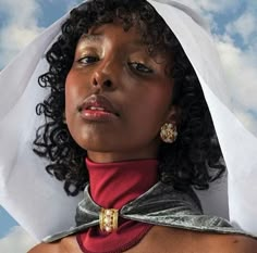 a woman with curly hair wearing a red and silver neck tie under a cloudy blue sky