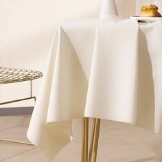 a white table cloth with gold legs and a plate on the top that has a croissant in it