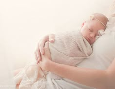 a woman holding a newborn baby wrapped in a white wrap and wearing a headband