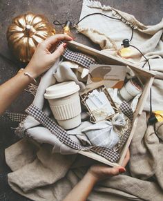 a woman is holding a box full of coffee and other items that are on the ground