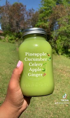 a hand holding a green jar with pineapple cucumber celery apple ginger on it