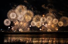 fireworks are lit up in the night sky over water and land, with dark clouds