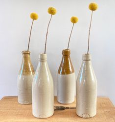 three vases with yellow flowers in them on a wooden table next to a white wall