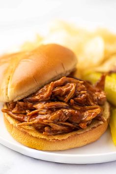 a pulled pork sandwich with pickles and potatoes on a white plate, ready to be eaten