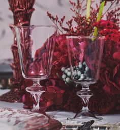 two wine glasses sitting on top of a table next to red flowers and other decorations