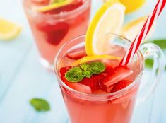 two glasses filled with ice and strawberries next to lemon wedges, mint and lime slices