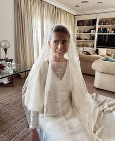 a woman sitting on top of a bed wearing a white veil over her head and dress