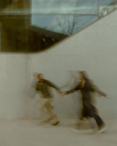 two people are holding hands while walking down the street in front of a white wall