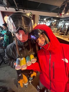 two people standing next to each other wearing ski gear and holding drinks in their hands