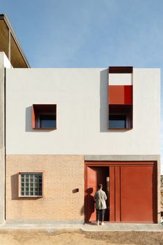 a man standing in front of a red and white building with two windows on each side