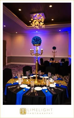 a table set up for a formal function with blue flowers and candles on the tables