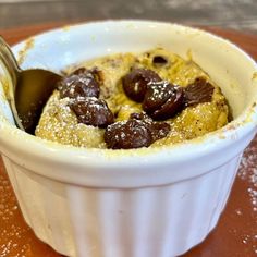 a white bowl filled with pudding on top of a wooden table next to a spoon