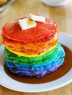 a stack of pancakes sitting on top of a white plate next to a rainbow cake