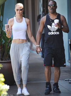 a man and woman holding hands while walking down the street with drinks in their hand