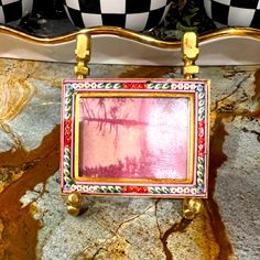 an ornately decorated mirror hanging on the side of a marble counter top with gold accents