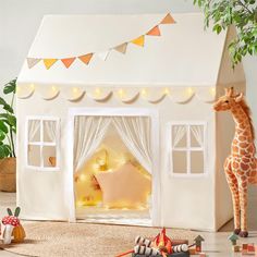 a giraffe standing in front of a doll house with lights on the windows