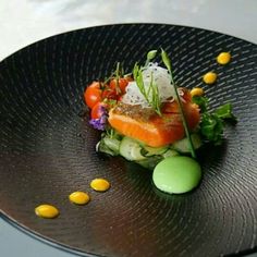 a black plate topped with lots of food on top of a wooden table next to an egg