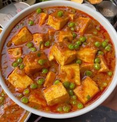 a bowl filled with tofu and peas on top of a table