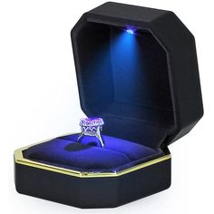 an open box with a ring in it on top of a white surface and blue light coming from the inside