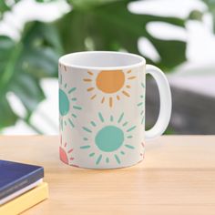 a coffee mug sitting on top of a wooden table next to a book and plant