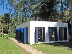 a small white building with blue shutters in the grass