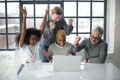 group of people standing around a white table in front of a window with their arms up