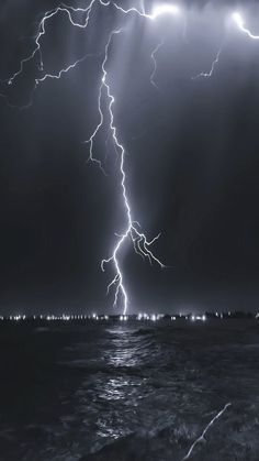 a black and white photo of lightning striking over the ocean with bright lights in the sky