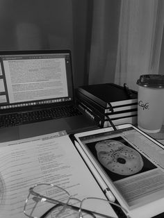 a laptop computer sitting on top of a desk next to a stack of books and glasses