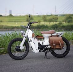 a white moped parked on the side of a road next to a lake and grass