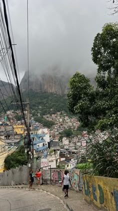 two people are walking up the side of a hill with graffiti on it and there is a mountain in the background