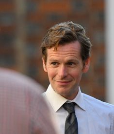 a man wearing a white shirt and black tie looking at another person in the background