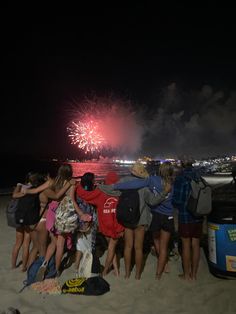 a group of people standing on top of a sandy beach next to the ocean with fireworks in the sky