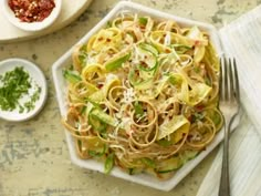 a white plate topped with pasta and vegetables next to a bowl of parmesan cheese