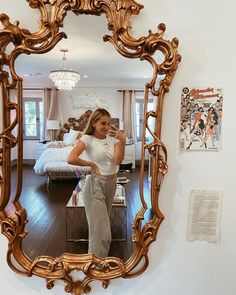 a woman taking a selfie in front of a gold framed mirror on the wall