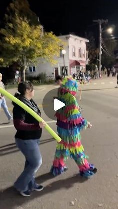 two people are walking down the street with some decorations on their head and one person is holding a large yellow stick