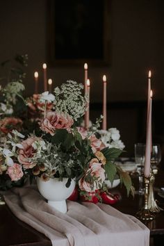 a table topped with flowers and candles next to a white vase filled with greenery