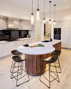 an island in the middle of a kitchen with stools and lights hanging from it