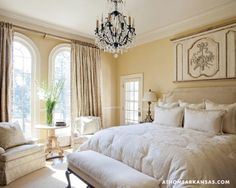 a large bed sitting in a bedroom next to two chairs and a chandelier