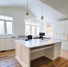 a large kitchen with white cabinets and wood floors, along with an island in the middle