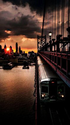 a train traveling across a bridge next to a river under a cloudy sky at sunset